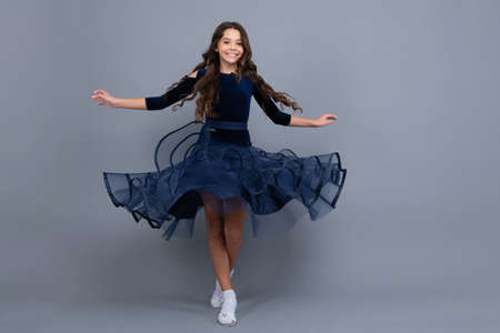 Full length teenager with movement dress. Young teen child with flowing skirt. Teen girl fluttering ball dress in motion, isolated on gray. Happy girl face, positive and smiling emotions.の写真素材