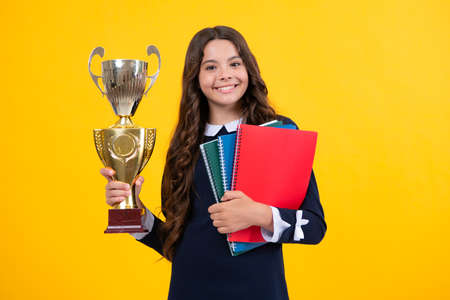 Schoolgirl in school uniform celebrating victory with trophy. Teen holding winning prize on yellow...