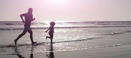 Silhouette of father and son run on summer beach outdoor, banner poster with copy space, dad and child having fun.の写真素材