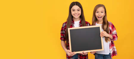 School girls friends. happy children in casual checkered hold school blackboard for copy space. Portrait of schoolgirl student, studio banner header. School child face, copyspace.の写真素材