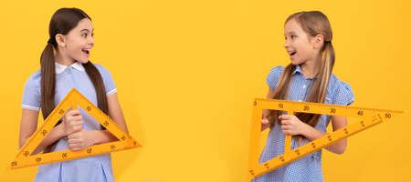 School girls friends. Happy school age children hold triangular rulers for geometry lesson, back to...