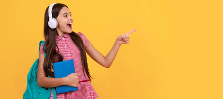 amazed school teen girl in headphones point finger on copy space, back to school. Horizontal isolated poster of school girl student. Banner header portrait of schoolgirl copy space.の写真素材