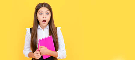 Surprised girl child hold school book yellow background. Portrait of schoolgirl student, studio banner header. School child face, copyspace.の写真素材