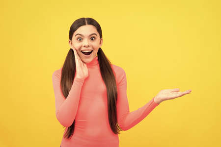 surprised child presenting product on copy space on yellow background, big saleの写真素材