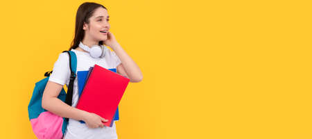 Female student. happy young girl with backpack and headphones hold workbook on yellow background,...