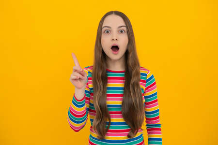 Amazed surprised emotions of young teenager girl. Funny teenager child over isolated yellow background showing and pointing up with finger number one.の写真素材