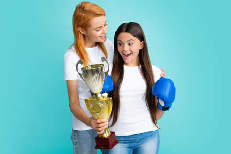 Woman power. Sportive young woman and her daughter wearing boxing gloves, holding winning prize, showing trophy, emotional excited and happy.の写真素材