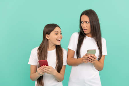 indignant mother and daughter chatting on smartphone on blue backgroundの写真素材