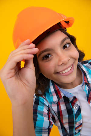 Close up portrait of child builder in helmet. Teenage girl on repairing work isolated on yellow background. Kids renovation concept.の写真素材