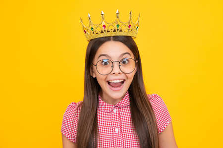 Amazed teen girl. Little queen wearing golden crown. Teenage girl princess holding crown tiara. Prom party, childhood concept. Excited expression, cheerful and glad.の写真素材