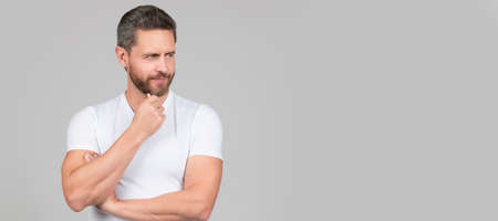 Serious thoughtful man in white tshirt stroke chin thinking grey background, think. Man face portrait, banner with copy space.の写真素材
