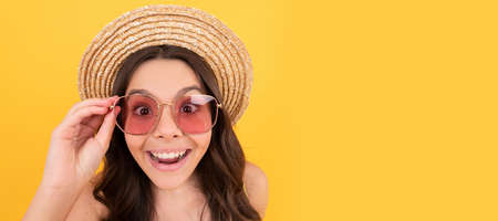 surprised kid in summer straw hat and glasses has curly hair on yellow background, summer sales. Child face, horizontal poster, teenager girl isolated portrait, banner with copy space.の写真素材