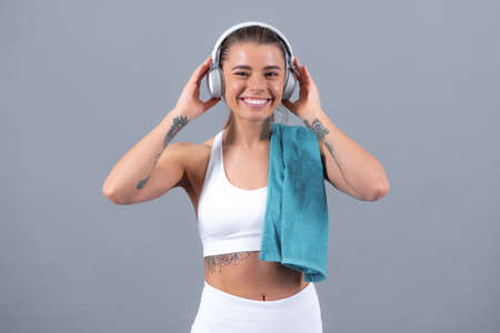 Young fitness woman runner with headphone and towel, isolated on gray background. Dynamic movement.の写真素材