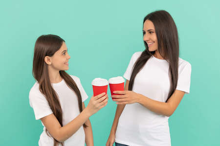 happy mother and daughter hold takeaway coffee on blue background. cheers
