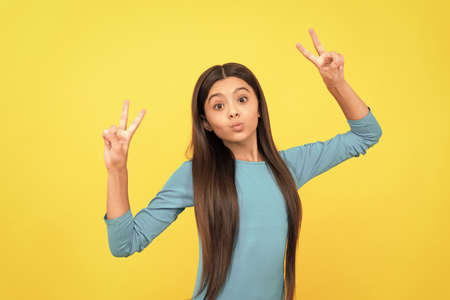 face portrait of child on yellow background. express positive emotions. peace gesture.の写真素材