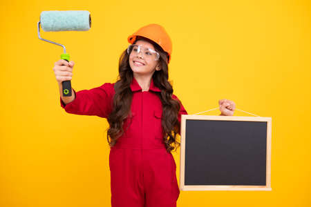 Little builder expert in helmet on construction site. Teen girl painter with painting brush tool or...