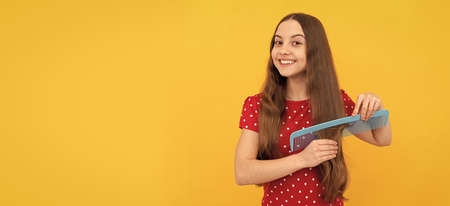 happy teen girl brushing long hair with hair brush on yellow background, copy space, hairdresser