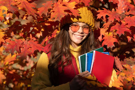Autumn teenager girl portrait in fall autumn leaves. happy kid hold workbook on autumn leaves background. back to schoolの写真素材