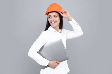 Young beautiful architect woman in hard hat helmet hold laptop computer over gray background. Female builder in helmet for advertising sign.の写真素材