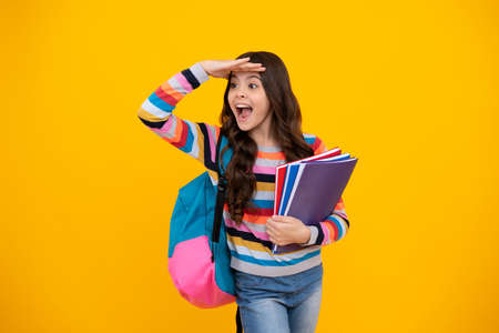 Amazed teenager. Schoolchild, teenage student girl hold book on yellow isolated studio background....