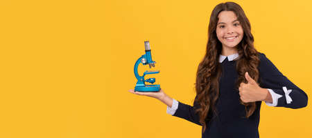 cheerful teen girl hold microscope for education on yellow background showing thumb up, chemistry....
