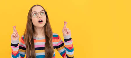 schoolgirl nerd child in eyeglasses for vision cross fingers making a wish, wish. Child face,...