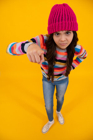 Beautiful teen girl in a winter hat and a warm sweater. A child on a yellow isolated background. Unhappy sad teenager girl.の写真素材