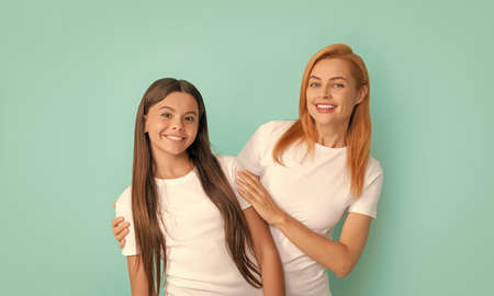 loving cheerful mother embrace daughter in white shirts on blue background, happinessの写真素材
