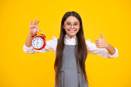 Teen girl holding clock over yellow background. Early morning, daily schedule. Child checking time. do not be late. Punctual kid with alarm. Deadline time. Happy face.の写真素材