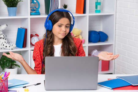 Funny face. School girl student sitting at the table, using laptop when studying. Happy girl face,...