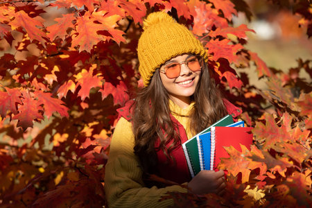 Autumn teen child girl portrait, fall leaves concept. glad child hold workbook on autumn leaves backgroundの写真素材