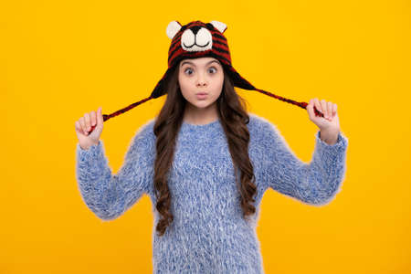 Modern teen girl wearing sweater and knitted hat on isolated yellow background. Funny face.の写真素材