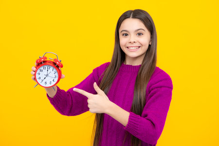 Portrait of teenage girl with clock alrm, time and deadline. Studio shot isolated on yellow...