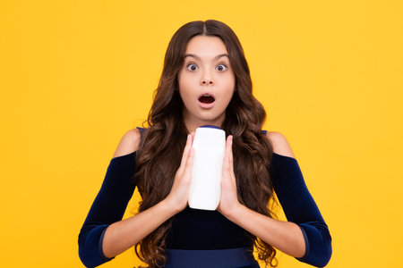 Child with shampoo conditioner. Daily cosmetic care. Teenager kid 12, 13, 14 years old hold bottle of hair and skin care. Beauty health and cosmetics. Surprised teenager girl.の写真素材