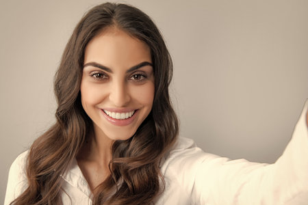 Studio portrait of beautiful smiling woman making selfie, photographing herself over gray background.の写真素材