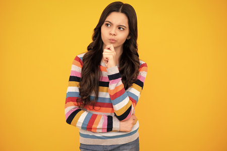 Thoughtful teenager girl touch chin and thinking, pensive child making idea, posing isolated on yellow isolated background. Thinking teenager girl, thoughtful emotion.の写真素材