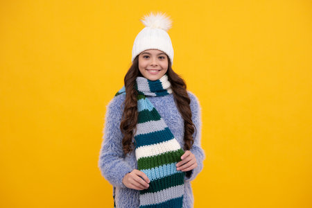 Teenager girl with winter hat over isolated yellow background. Winter christmas holidays, new year mood. Kids warm clothes. Happy girl face, positive and smiling emotions.の写真素材