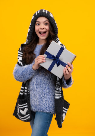 Happy teenage girl. Teenager child holding gift box on isolated yellow background. Gift for kids birthday. Christmas or New Year present box. Smiling kids emotions.の写真素材