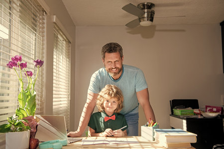 cheerful daddy writing school homework with his kid son in classroom, fatherhoodの写真素材