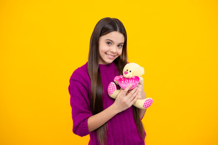 Teen with toy teddy bear with love heart for valentines day. Teen girl in casual clothes hold soft toy for birthday on yellow background. Kid spending time with her toys.の写真素材