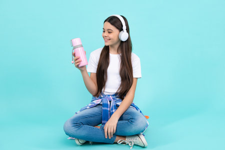 Happy teenager child girl with thermos bottle, hydration, isolated on blue background.の写真素材
