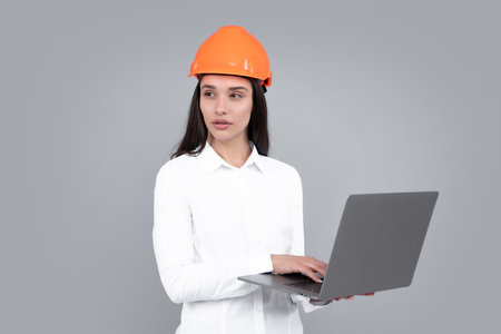 Young woman construction manager. Woman builder isolated portrait with protect helmet and laptop computer. Gray background, copy space.の写真素材
