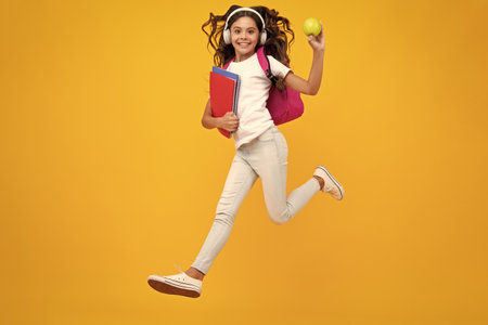 School girl, teenage 12, 13, 14 years old in headphones and books on isolated studio background. School kids with backpack.の写真素材