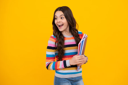 Amazed teenager. Teen girl pupil hold books, notebooks, isolated on yellow background, copy space....