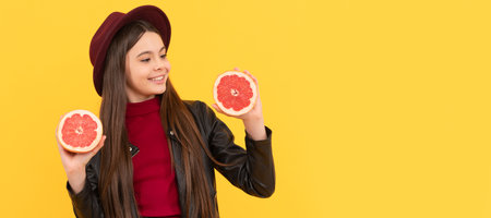 happy teen girl in hat and leather jacket hold cut grapefruit. Child girl portrait with grapefruit orange, horizontal poster. Banner header with copy space.の写真素材