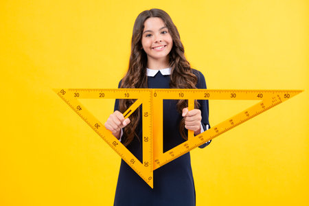 Measuring school equipment. Schoolgirl holding measure for geometry lesson, isolated on yellow...