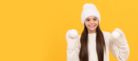 happy teen girl ion winter hat and gloves hold snowballs on yellow background, christmas. Banner of christmas child girl, studio kid winter portrait with copy space.の写真素材