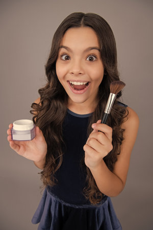 Beauty, make up and kids cosmetics. Teenage girl with brush applying blush to face isolated on grey studio background. Excited face, cheerful emotions of teenager girl.の写真素材
