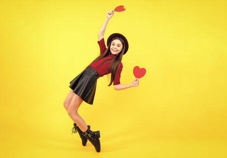 Cheerful lovely romantic teen girl hold red heart symbol of love for valentines day isolated on yellow background. Excited teenager, glad amazed and overjoyed emotions.の写真素材