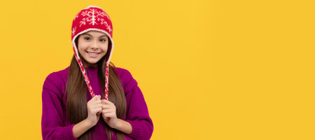 smiling child in winter hat on yellow background, knitwear. Banner of christmas child girl, studio...